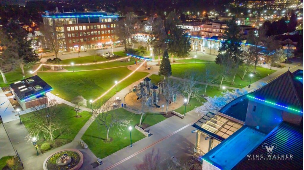Aerial nighttime view of a downtown park in Puyallup with multicolored lights and active pedestrians.