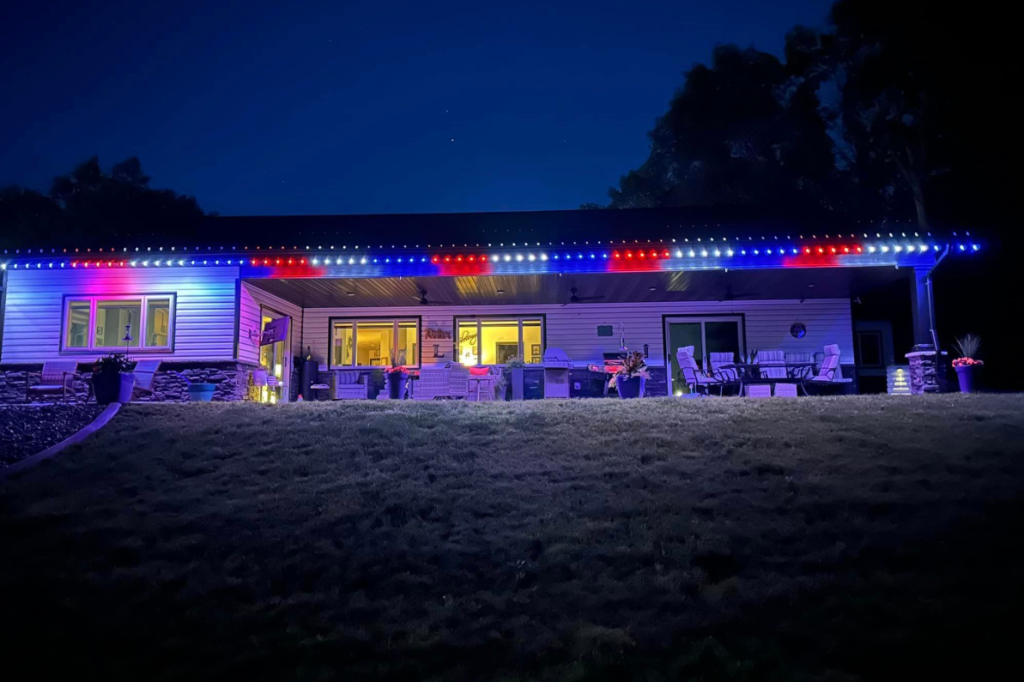 red, white, and blue permanent lighting on the outside of a white, single-story home with a porch in the front