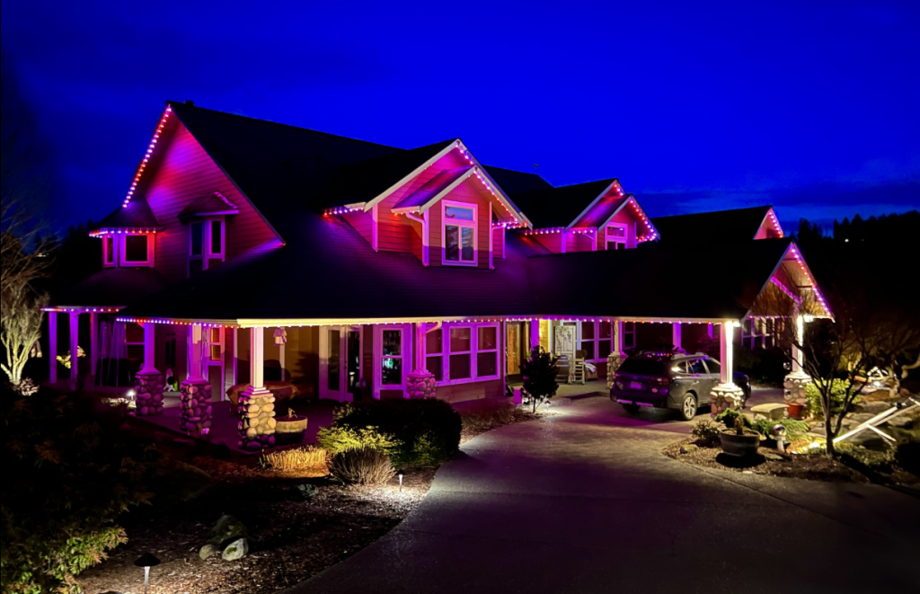 A large two-story house with a car out front in the driveway, showing off its permanent lighting ROI with a gorgeous exterior lighting system