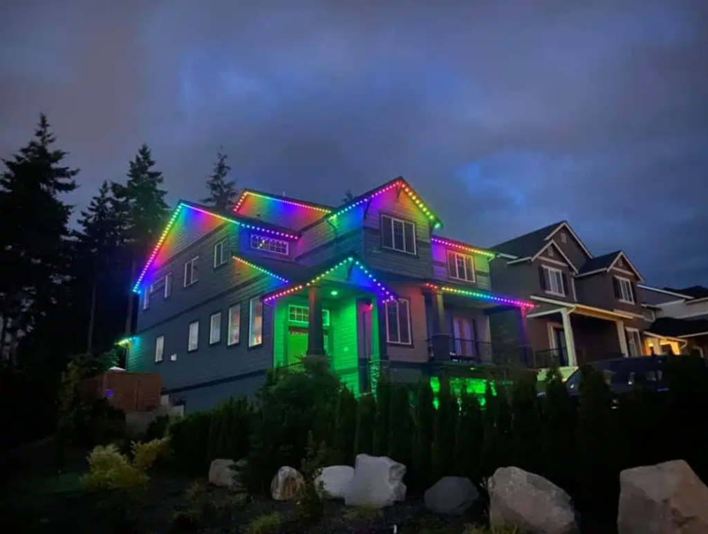 A big gray three story home with permanent exterior lighting glowing rainbow colors