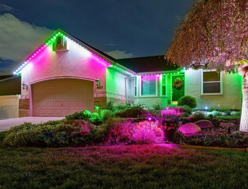 Outside of a home with pink, green and white lights on the exterior and in the yard 