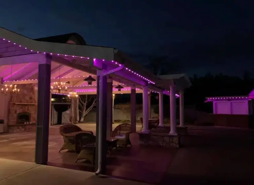 backyard patio with a roof and exterior lit up with pink permanent exterior lighting 