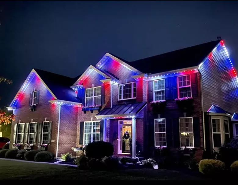 permanent exterior lighting on a two-story home glowing red, white, and blue