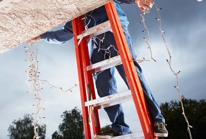 man on a ladder putting up Christmas lights on the outside of a home