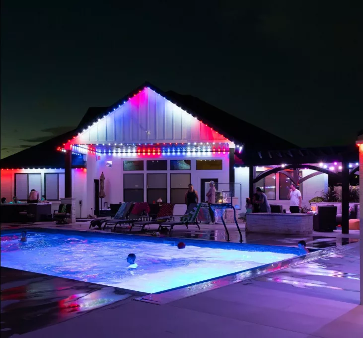 home exterior lighting glowing red, white, and blue, with people hanging out in the backyard and pool | permanent lighting vs smart bulbs
